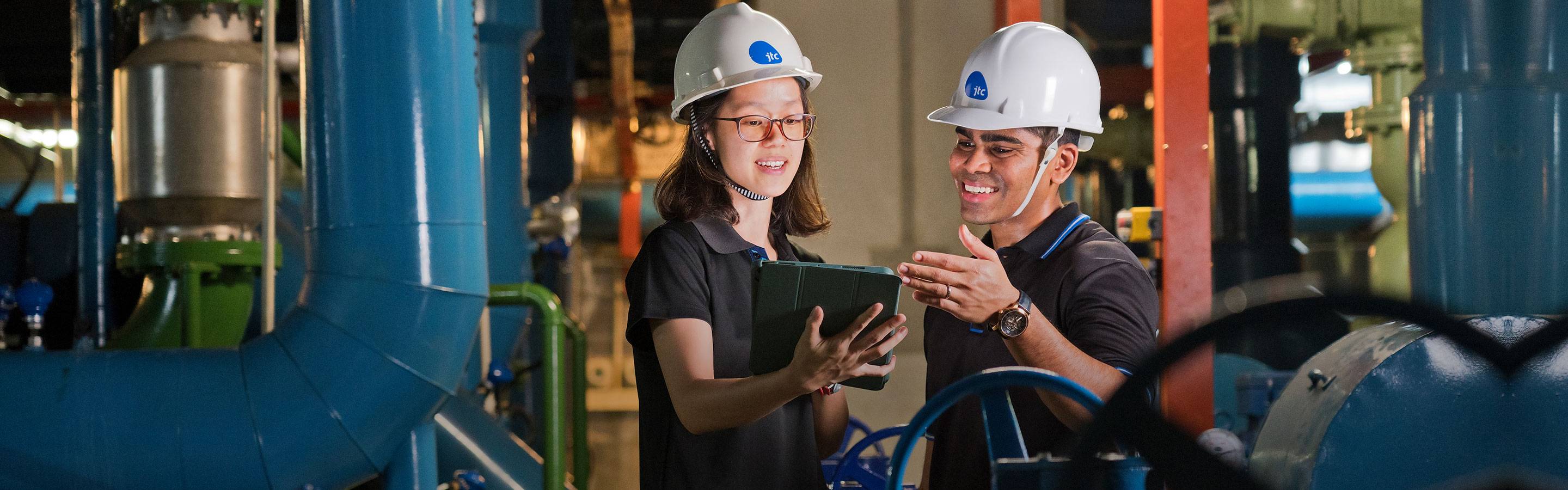 Two workers in hard hats conducting checks in an indoor facility