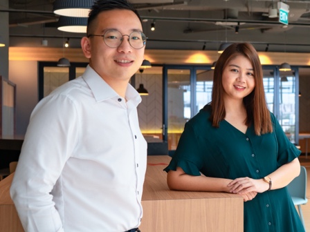 Two employees posing against a table in an office