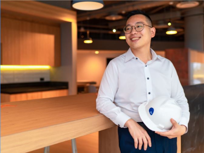 A JTC employee with a hard hat in his hand leans against a table