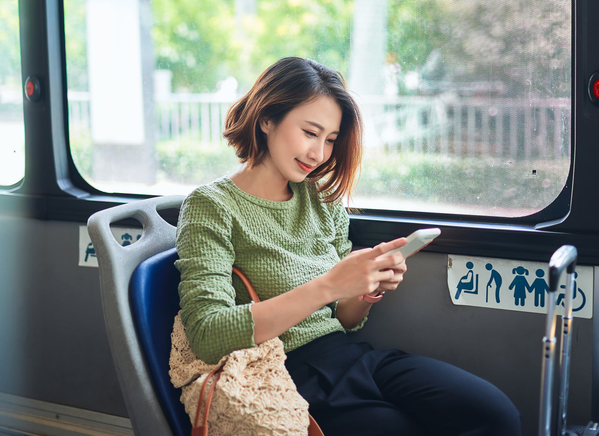 A smiling woman uses her phone while sitting in a bus