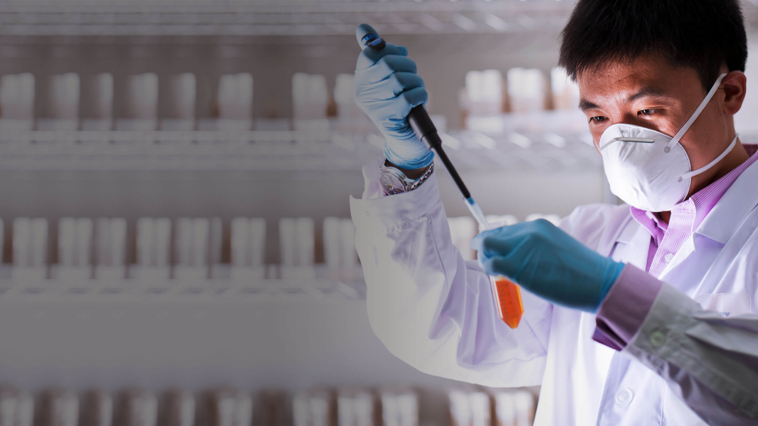 Scientist in a lab coat, gloves and mask examining a liquid in a laboratory