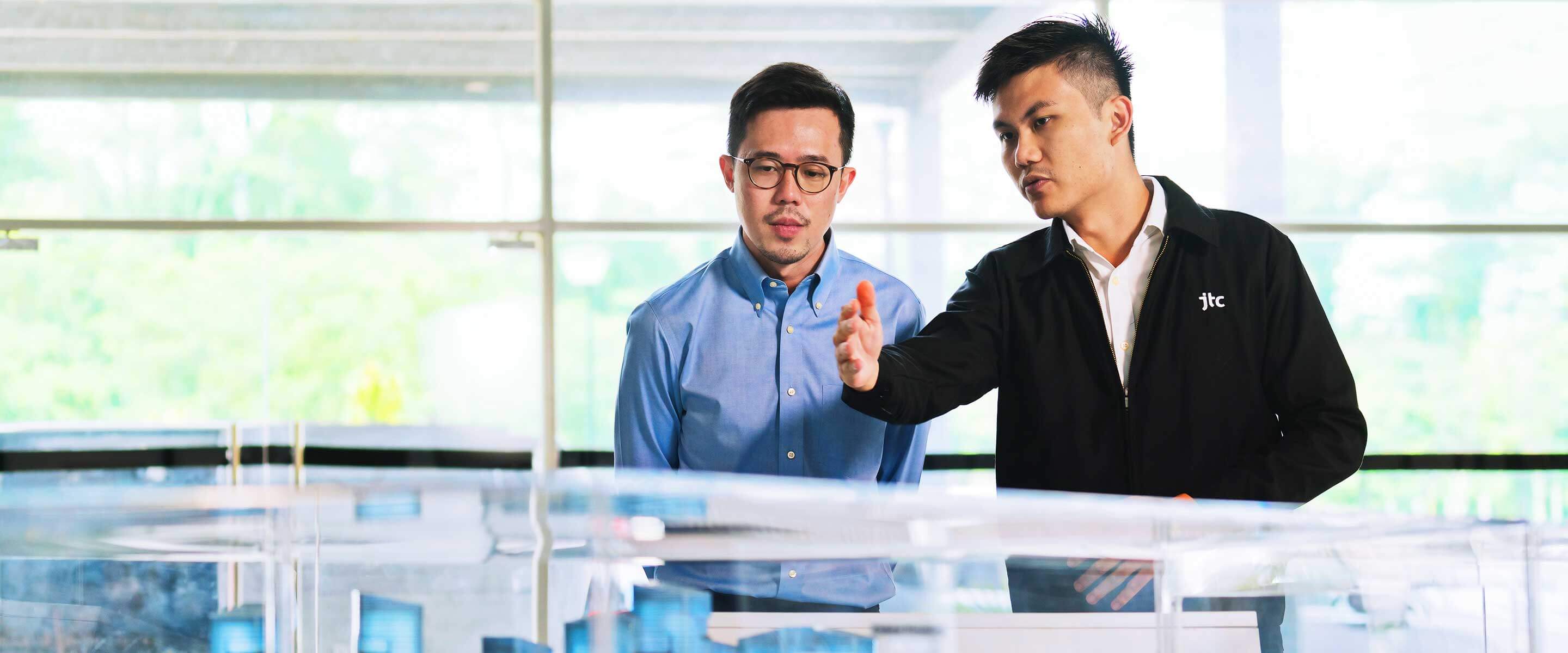 Two men having a discussion over a building model of a smart city